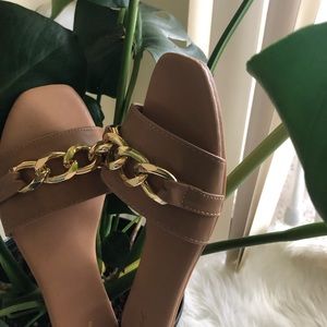 Neutral flat sandals with gold chain on top.